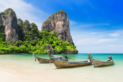 Longtail boats on a Thai beach beneath limestone cliffs.