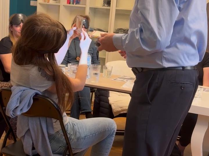A masked participant holding a card up while an instructor presents it, others waiting their turn.