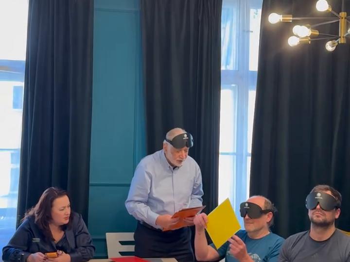 A yellow sheet held out to two masked participants seated at a table.