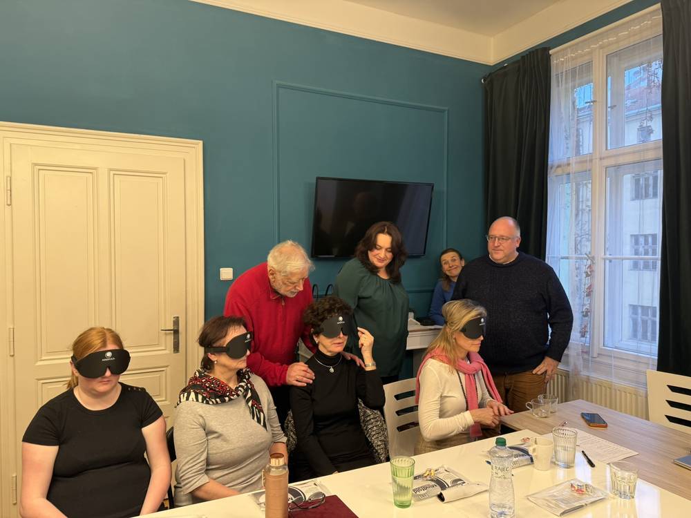 Mark Komissarov leaning in to work with three seated participants wearing blackout masks while others look on.