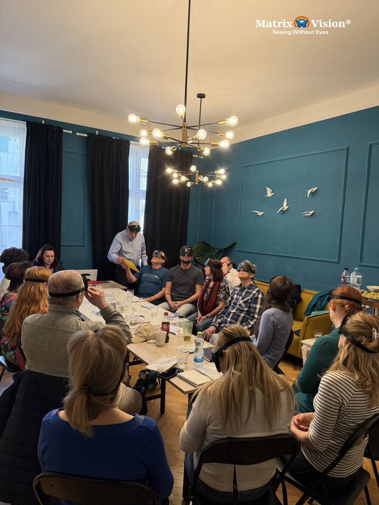 A full room of participants seated around a table, all wearing blackout masks, during a seminar session.